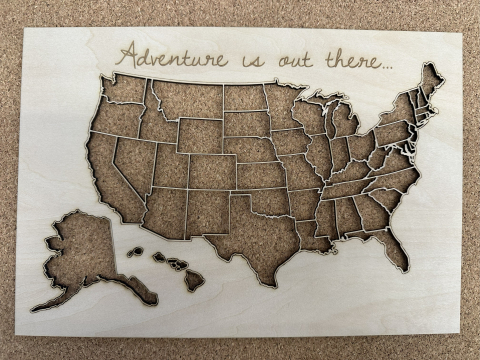 Image of a laser cut map of the United States of America with the words "Adventure is out there" engraved on top. 