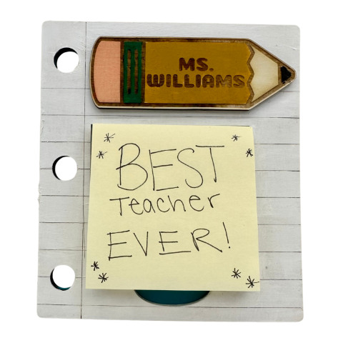 An image of a wooden block in the shape of paper with a wooden block in the shape of a pencil. There is a stack of sticky notes in the middle with the phrase, "Best Teacher Ever!"
