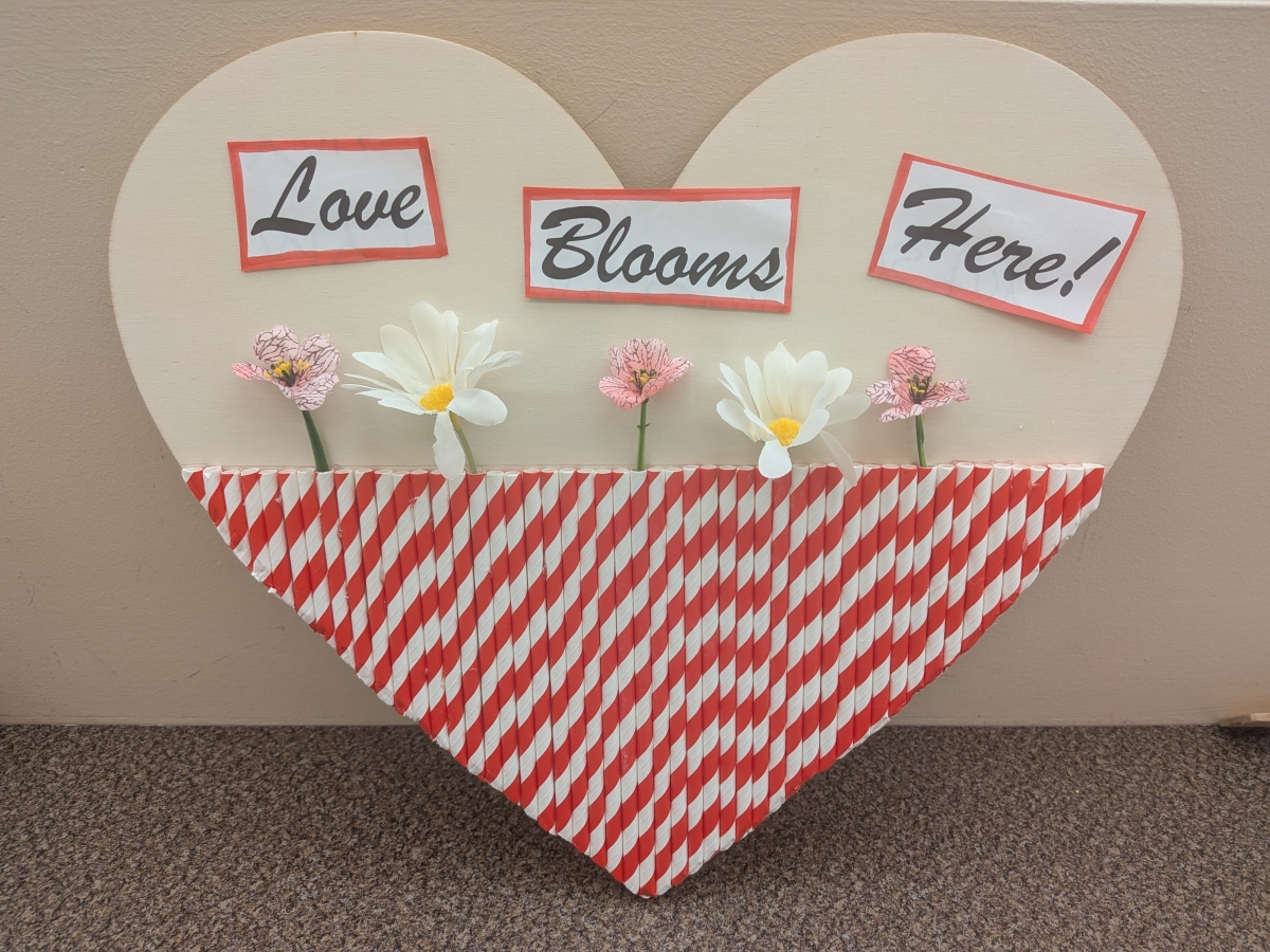 Wood heart decorated with striped straws and flowers.
